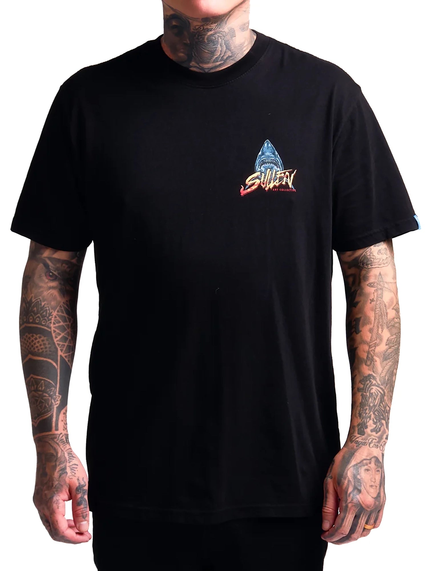 A man wearing a black short-sleeve t-shirt with a small multicolor graphic on the left chest. The graphic features a blue shark fin above the stylized red and white 'SHARK' brand logo.