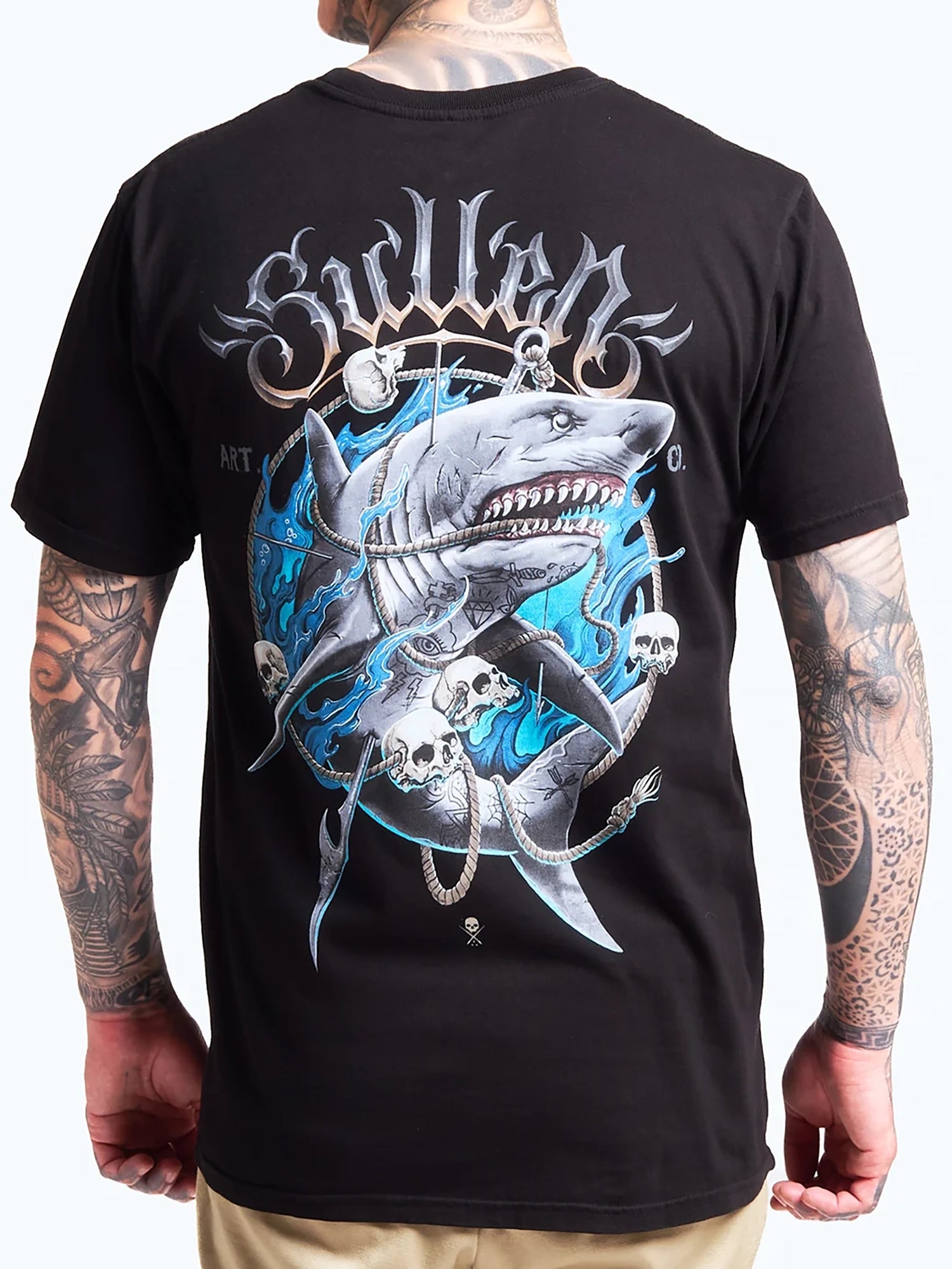 A man wearing a black Sullen brand t-shirt, shown from the back. The shirt features a large graphic print of a shark, skulls, and blue flames, with the word 'Sullen' in a stylized font above the design.