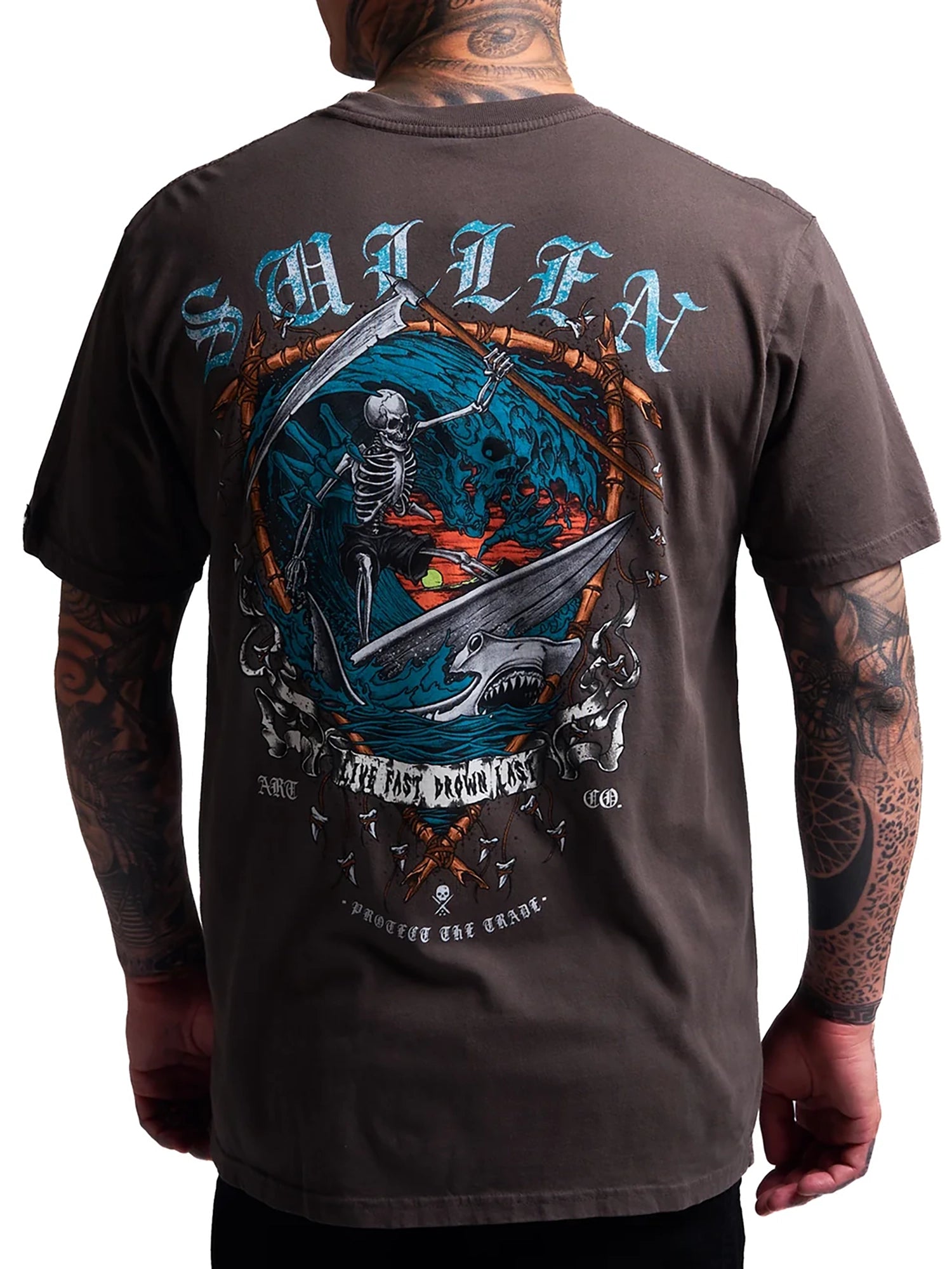 A man wearing a dark brown t-shirt, viewed from the back. The shirt features a large graphic print of a skeleton scythe holding a shark, with the word 'SMILEN' in light blue gothic lettering above and 'ALL LOST ARE FORGED' in white below.