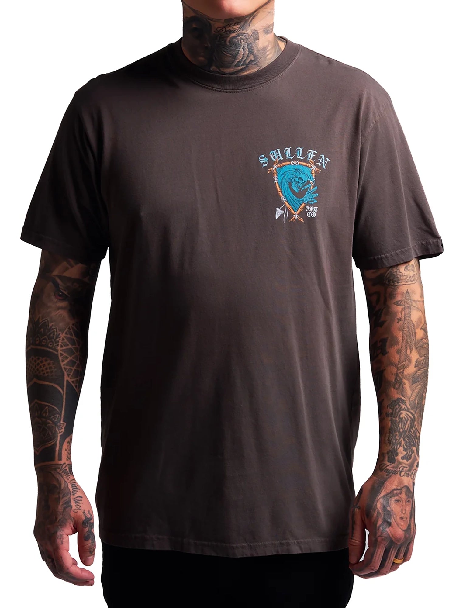 A man wearing a dark brown t-shirt with a small blue and white chest graphic that reads 'SALTS & X'. The photo is cropped from the neck down, showing tattooed arms and hands against a plain white background.