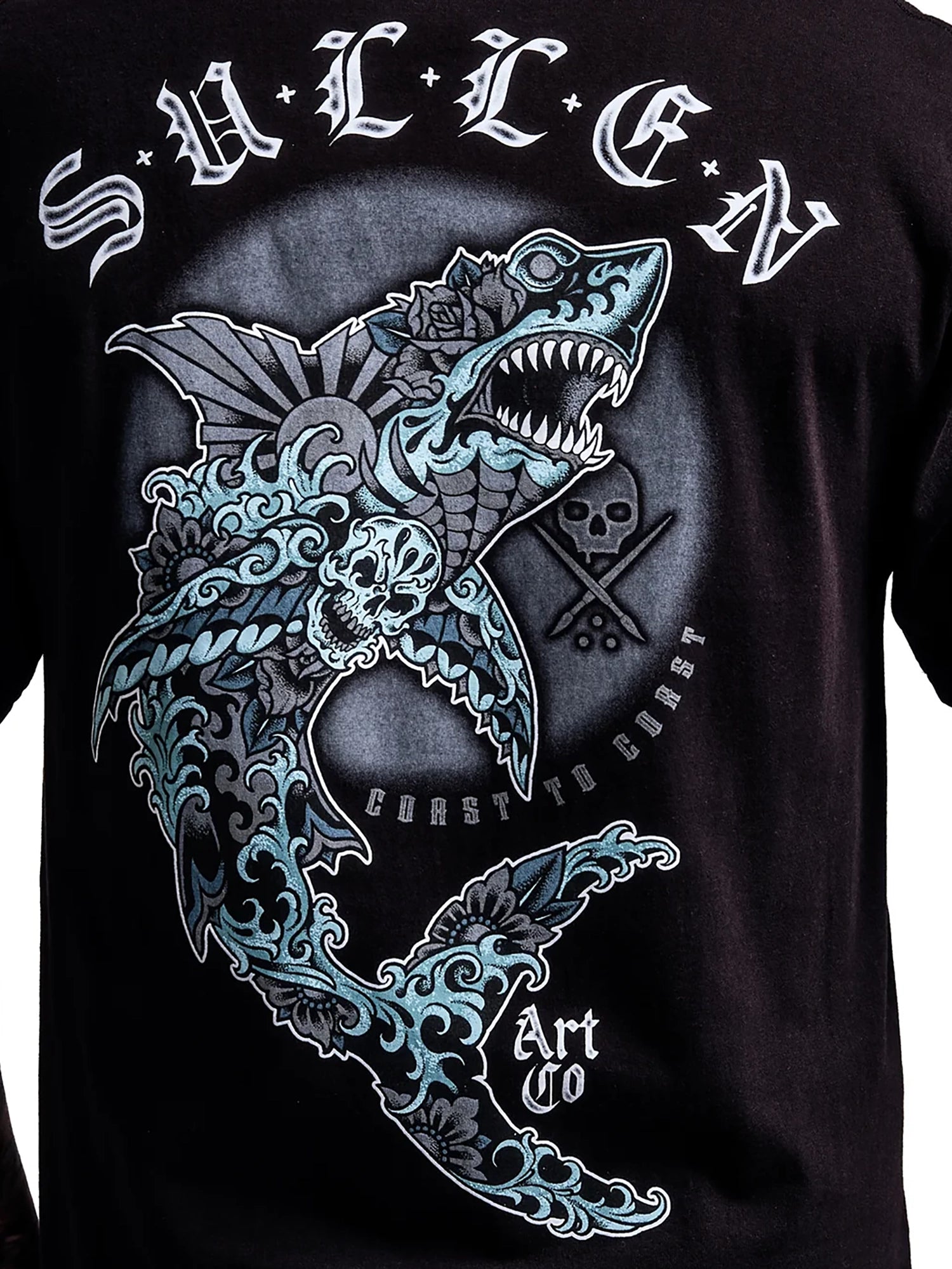 A close-up of a black t-shirt featuring a large graphic print of a stylized shark with blue and white wave details, skulls, and the text 'SALTS' and 'Coast to Coast Art Co'.